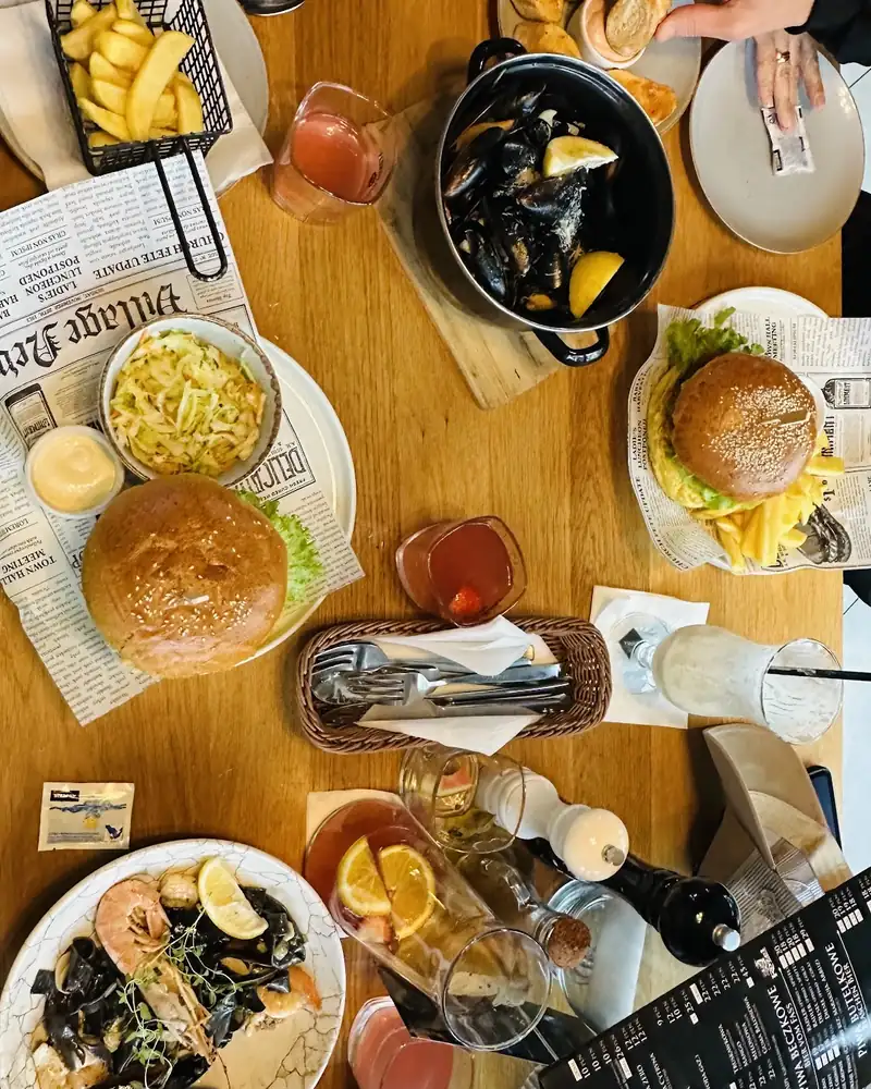 Stół pełen dań: mule, burger, makaron z owocami morza, frytki